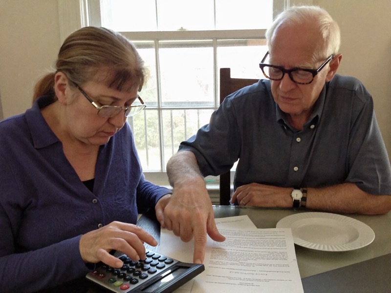 A retired couple at their dining table checking a loan document with a calculator
