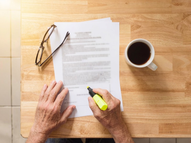 Hands highlighting lines on a contract next to reading glasses and coffee