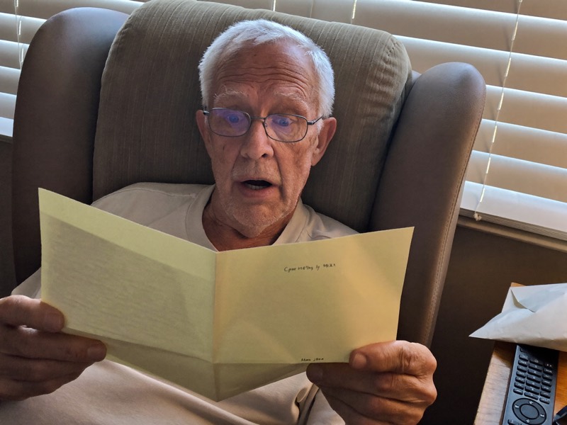 A man in his recliner reading a letter with a surprised look
